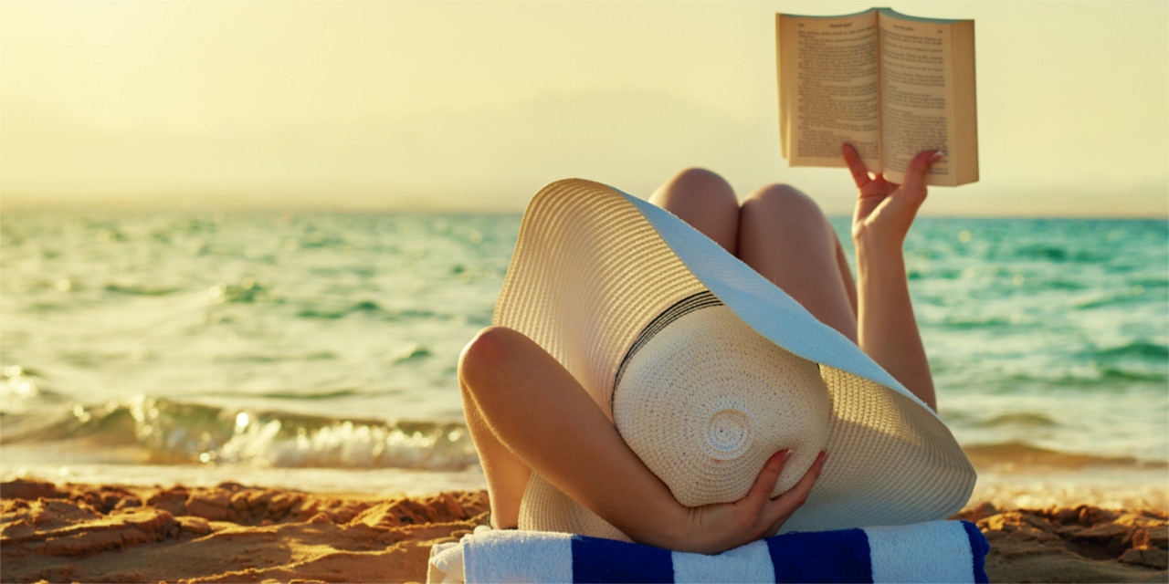 kvinde med solhat læser bog på strand