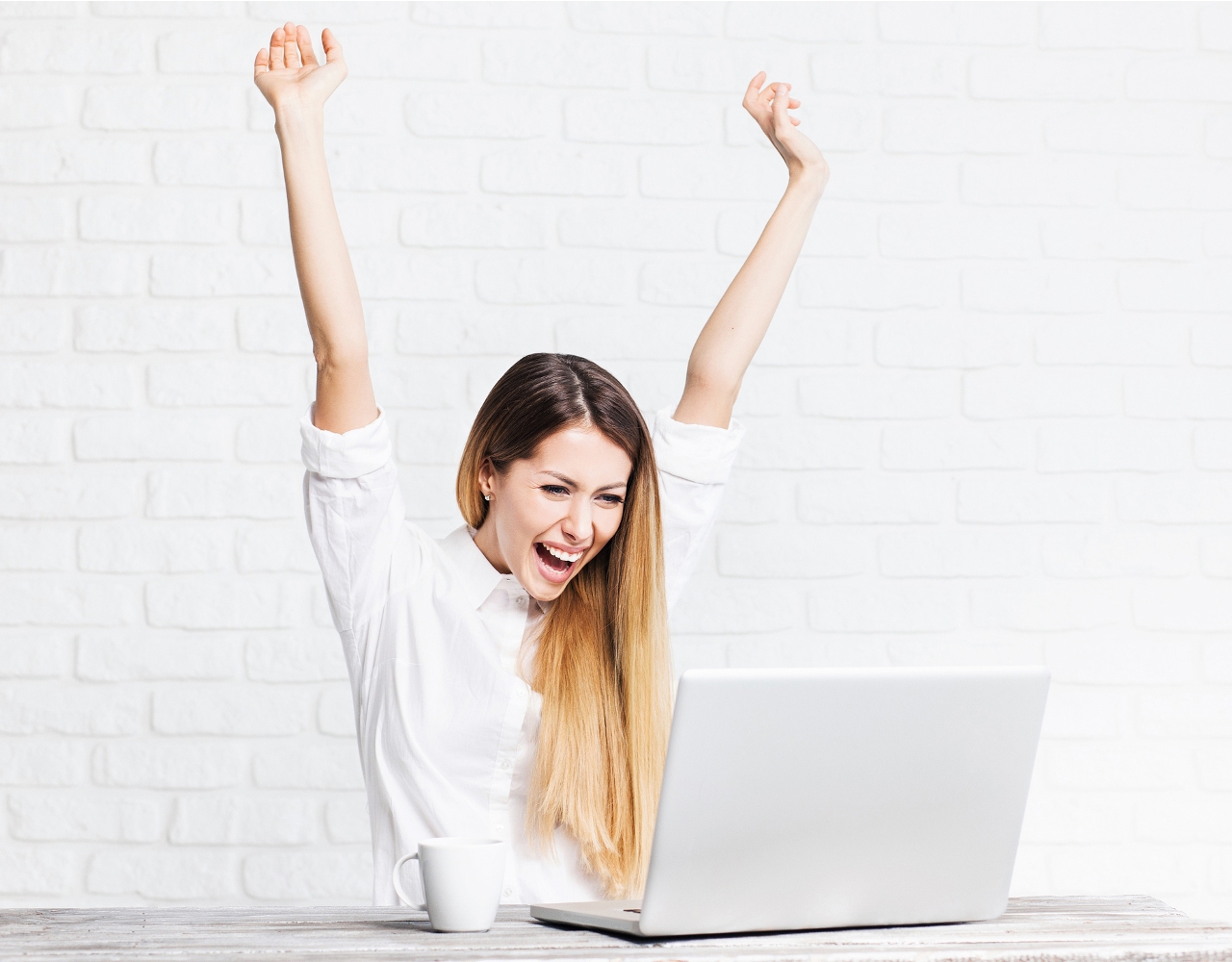 glad kvinde med armene over hovedet foran computer